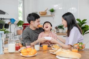 actividades juntos durante las vacaciones. padres e hijos están comiendo juntos durante las vacaciones. el niño se burla de su padre dándole pan y verduras. foto