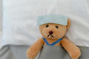 Teddy bear lying sick in bed. Teddy bear with antipyretic patch photo