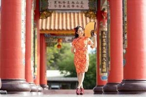 mujer asiática con vestido rojo cheongsam qipao sosteniendo un abanico de papel mientras visita el templo budista chino durante el año nuevo lunar por el concepto de cultura tradicional foto
