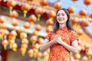 mujer asiática con vestido rojo cheongsam qipao está rindiendo respeto y gratitud dentro del templo budista chino durante el año nuevo lunar por la mejor bendición y el concepto de buena suerte foto