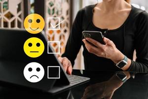 concepto de evaluación del servicio al cliente. mujer mostrar cara sonrisa emoticono mostrar en pantalla virtual desde la mano.mirando el teléfono inteligente, la tableta y la computadora portátil foto