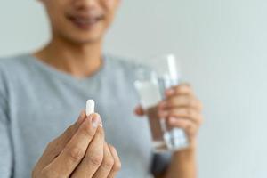 primer plano de un hombre que sostiene un suplemento dietético o un medicamento y un vaso de agua listo para tomar el medicamento. conceptos de salud de las personas. foto