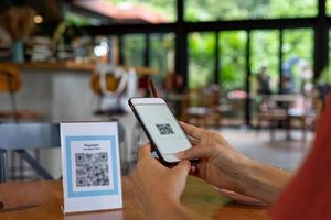 los hombres usan teléfonos para escanear un código qr para seleccionar un menú o escanear para recibir un descuento o pagar comida y bebida dentro de un café. usar el teléfono para transferir dinero o pagar en línea sin concepto de efectivo. foto