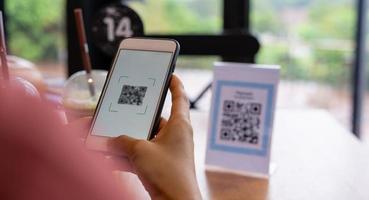 los hombres usan teléfonos para escanear un código qr para seleccionar un menú o escanear para recibir un descuento o pagar comida y bebida dentro de un café. usar el teléfono para transferir dinero o pagar en línea sin concepto de efectivo. foto