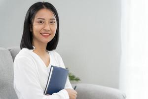 empresaria asiática sonriendo y sosteniendo un libro en la oficina. hermosa y guapa mujer asiática se sienta en el sofá. retratos femeninos. foto