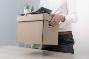 A businessman holds a box for personal items after sending a resignation letter to an executive or boss. Include information about resignation and vacancies and job changes. photo