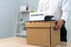 A businessman holds a box for personal items after sending a resignation letter to an executive or boss. Include information about resignation and vacancies and job changes. photo