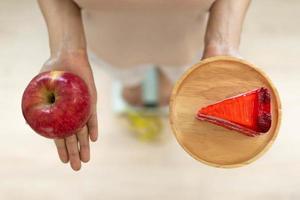 Women are choosing the right food for good health. Women are fasting. Comparison options between donuts and  apples during weight measurement on digital scales. Diet concept. photo