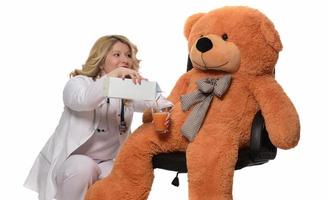 Close up of young female doctor in uniform checking teddy bear with stethoscope at clinic. Confident medical practicitioner or healthcare worker examining teddy bear at hospital photo