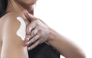 woman applying moisturizer cream on her shoulder, isolated on white photo