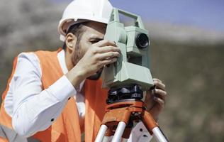 trabajador ingeniero agrimensor haciendo mediciones con equipos de teodolito en el sitio de construcción durante las obras viales foto