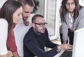 Multi-tasking businessman working in the office. He is using touchpad while reading an e-mail on laptop and taking notes on the paper. photo