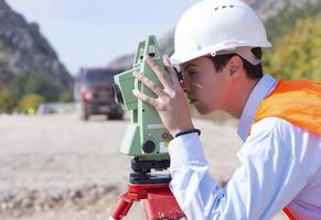 trabajador ingeniero agrimensor haciendo mediciones con equipos de teodolito en el sitio de construcción durante las obras viales foto