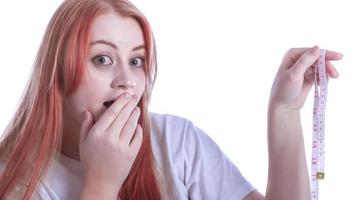 Smiling beautiful confused young redhead plus size body positive woman 20s wearing white casual t-shirt hold measure tape looking camera photo