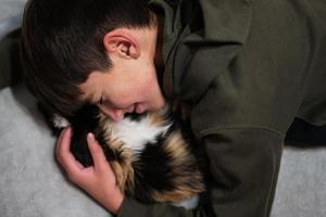 Teenager boy with kitty lying on the sofa. Children's love for pets. photo