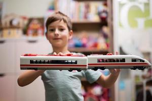 niño sostenga el tren de alta velocidad de juguete en las manos en la habitación de los niños. foto