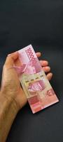 retrato de billetes de banco indonesios rp. 100.000 en mano. moneda rupia indonesia aislado sobre fondo negro foto