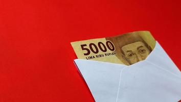 Indonesian rupiah banknotes worth IDR 5,000 in a white envelope isolated on red background photo