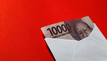 Indonesian rupiah banknotes worth IDR 10,000 in a white envelope isolated on red background photo