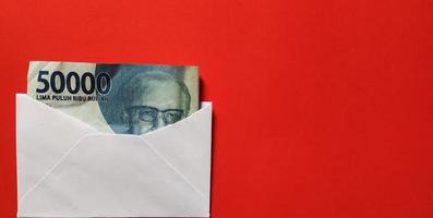 Indonesian rupiah banknotes worth IDR 50,000 in a white envelope isolated on red background. Free space photo