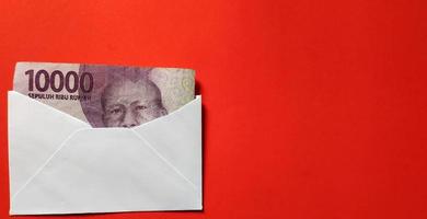 Indonesian rupiah banknotes worth IDR 10,000 in a white envelope isolated on red background photo