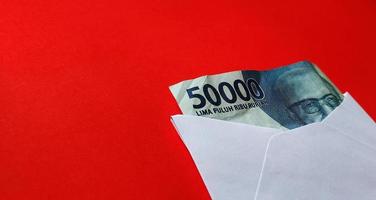 Indonesian rupiah banknotes worth IDR 50,000 in a white envelope isolated on red background photo