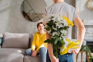 feliz día de la madre o de la mujer.hijo preparándose para sorprender a mamá con flores y un regalo foto