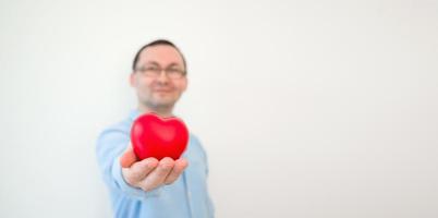 joven sonriente sosteniendo el corazón contra la pared blanca. banner de san valentín con lugar para texto foto