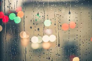 gotas de lluvia en la ventana y el fondo de las luces de la calle por la noche foto