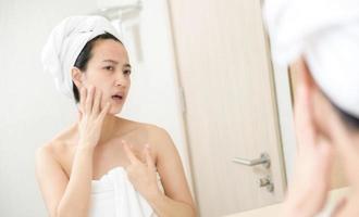 Problem skin. Concerned young asian women popping pimple on cheek while standing near mirror in bathroom. young asian women with acne photo