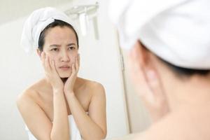 Problem skin. Concerned young asian women popping pimple on cheek while standing near mirror in bathroom. young asian women with acne photo