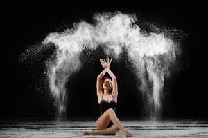 Young beautiful woman with spread flour on the air on a black background photo