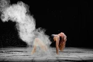 joven mujer hermosa con harina esparcida en el aire sobre un fondo negro foto