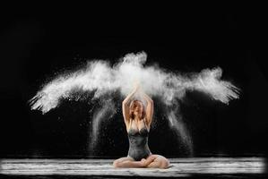 Young beautiful woman with spread flour on the air on a black background photo