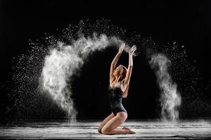 Young beautiful woman with spread flour on the air on a black background photo