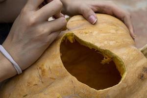 female carving large orange pumpkin for Halloween while sitting at wooden table at home photo