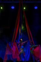 Professional aerialist circus performer on red bright aerial silks performs balance on a splits photo