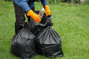 Closeup garbage collector worker hands hold plastic bottles to put into black garbage bags to recycle. Concept , Waste management. Environment problems. Daily chores. Throw away rubbish . photo