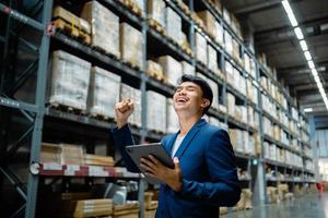 Portrait of a confident Asian businessman. Standing in a large warehouse. Wholesale, logistics, business, export. The manager inspects the goods at the warehouse. Logistics and export of business. photo