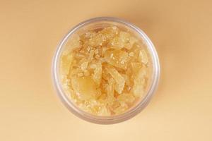 glass jar with golden cannabis wax, pieces of hardened resin of marijuana extract on an orange background photo