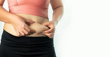 concepto de cuidado corporal, mano de mujer pellizcando su exceso de grasa abdominal, cuerpo de celulitis de mujer gorda y malsana aislado en fondo blanco foto