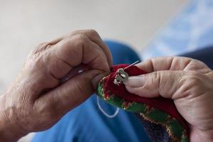 Old hand women sew hooks for attaching clothes. photo