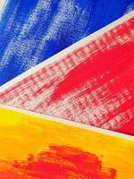 Three abstract drawings lie on surface, overlapping each other. Acrylic or gouache blue, red, yellow paint on texture paper. Partially visible, selective focus, close up, vertical image. photo