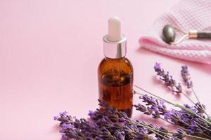 frasco cuentagotas y masajeador de piel facial con flores de lavanda sobre fondo de color foto