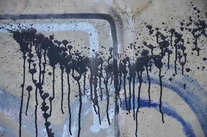 A photograph of a close-up of black paint spots on a concrete wall. Pouring paint on the wall in random order. The concept of graffiti and street art culture photo