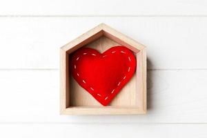 vista superior del corazón textil rojo en una casa sobre fondo de madera. concepto de hogar dulce hogar. día de San Valentín foto