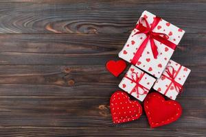 Valentine or other holiday handmade present in paper with red hearts and gifts box in holiday wrapper. Present box of gift on Dark wooden table top view with copy space, empty space for design photo