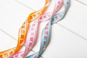 Close up of colorful measure tapes on wooden background. Perfect female figure measurements concept photo