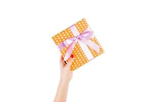 Woman hands give wrapped Christmas or other holiday handmade present in orange paper with purple ribbon. Isolated on white background, top view. thanksgiving Gift box concept photo