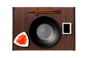 Empty round black plate with chopsticks for sushi, ginger and soy sauce on dark bamboo mat background. Top view with copy space for you design photo